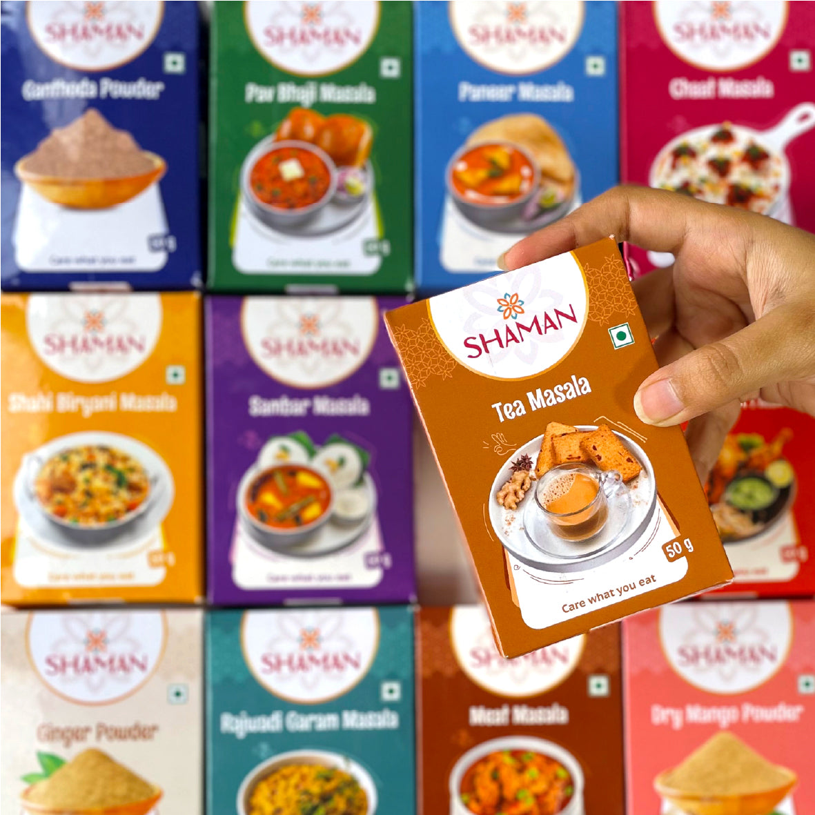 Hand holding a 'Shaman Tea Masala' packet with various other 'Shaman' product boxes in the background.